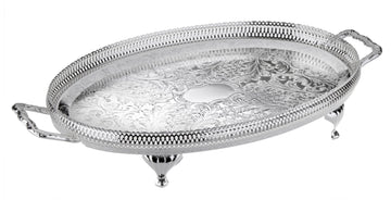 An oval-shaped silver-plated metal tray with handles and legs, featuring intricate designs on the surface.